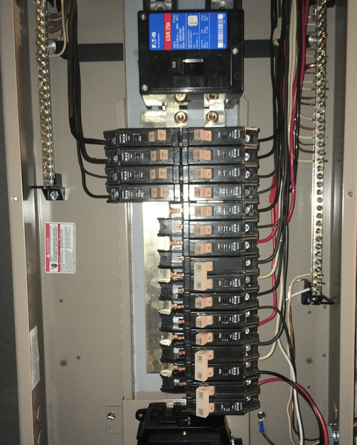 The image shows the interior of an electrical panel with multiple circuit breakers arranged vertically, connected wiring, and a digital monitoring device with a blue display screen at the top.